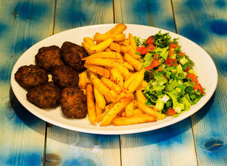 Meatball plate, french fries and salad, blue wooden background
