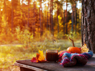 Outdoor recreation in October. Drink hot coffee in a Cup on a wooden table against the background of a colorful autumn forest. Romance and enjoy life