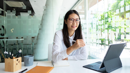 Cropped shot of female office worker smiling and looking into camera while working with tablet in...