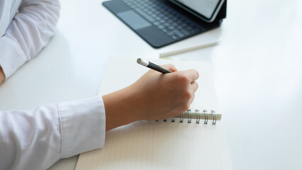 Cropped shot young businesswoman writing her project while holding a cup of coffee in office