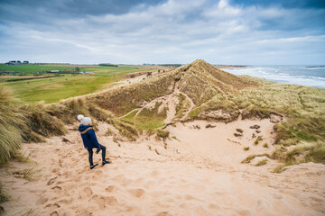 Girl looking out over dunes and coastal scene in Northumberland