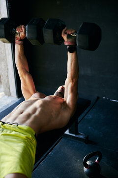 Shirtless fit young man working out in a garage with dumbells