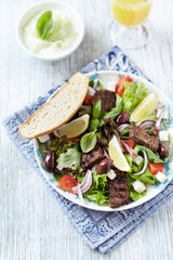 Tasty Salad with Grilled Beef Pieces, Cherry Tomatoes, feta Cheese and Kalamata Olives. Bright wooden background. Top view. 
