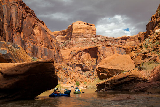 People paddle packrafts below high cliffs on Escalante River, Utah