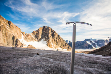Climbers ice axe in front of glacier and mountains.