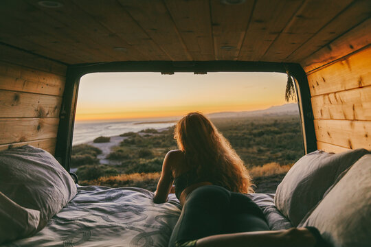 Young woman looking out to ocean from bed of camper van in Mexico.