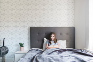 Young girl sitting in bed at home with a broken arm smiling