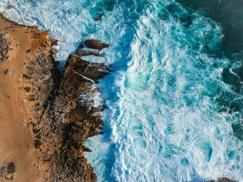 Aerial top view of sea waves hitting rocks on the beach with turquoise