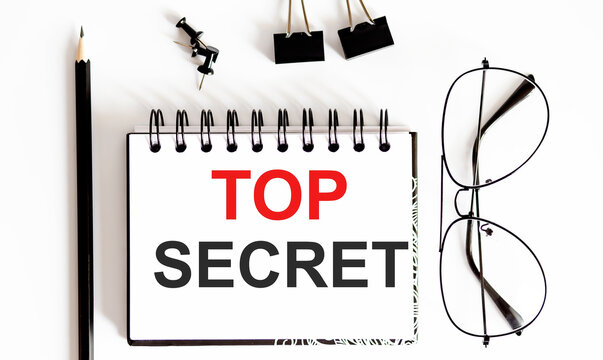 Top view ,pencil,glasses and notebook written TOP SECRET on white background.