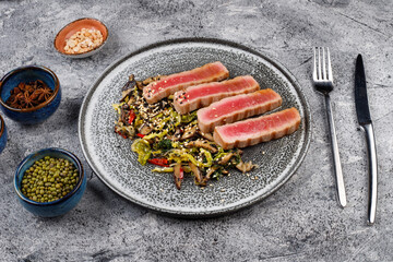grilled tuna steaks on a modern plate with a salad of mushrooms,vegetables and sesame seeds, top view