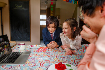 Smiling girl in fancy dress sits with family at table on zoom meeting