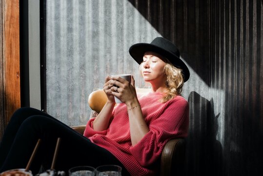 Portrait of woman sitting in cafe holding coffee cup enjoying sunlight
