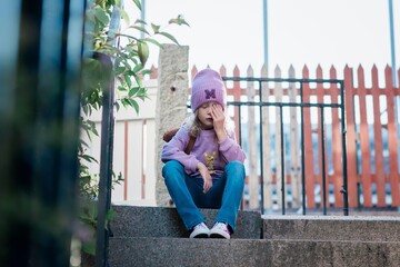 young girl looking stressed sat on a step waiting for school
