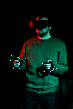 A young man plays with virtual reality equipment in a dark room