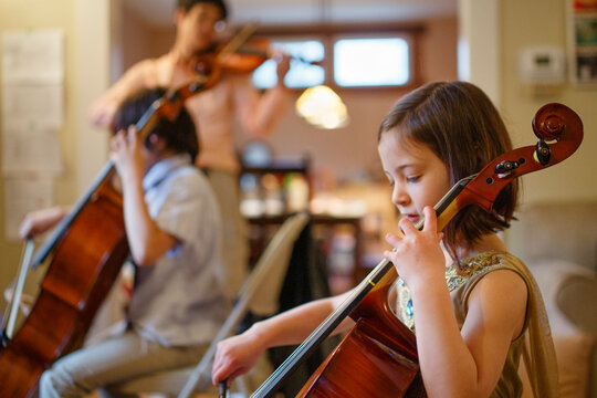 Father along with his kids practicing cello together in their living room