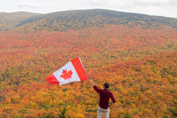 Autumnal view of a man with a lumberjack shirt holding a Canadian flag in the Mont-Megantic national park, Canada