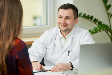 Fototapeta premium A caucasian doctor in a white lab coat is rejoicing in the success of the healing of a female patient in a hospital. A woman with long hair at an appointment in a doctor's office.