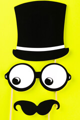 Top view image of funny masks on yellow background. Paper glasses, hat and mustache on bright background. Men's health awareness month. International Men's Day.