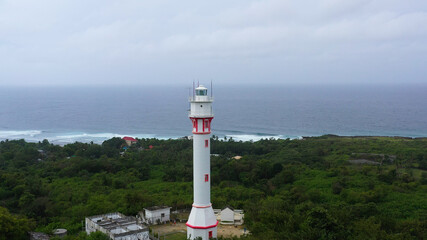 White tower lighthouse on a large island, top view. Rainforest hill and lighthouse tower. Bolinao Lighthouse, Luzon, Philippines. Summer and travel vacation concept.