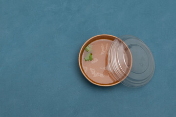 Bone broth with natural collagen in a disposable paper bowl. Food delivery or takeaway. Blue background, copy space