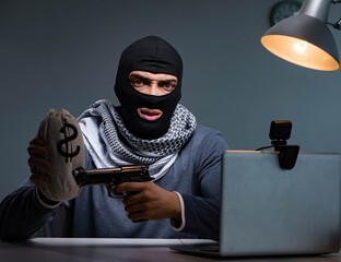 Terrorist burglar with gun working at computer