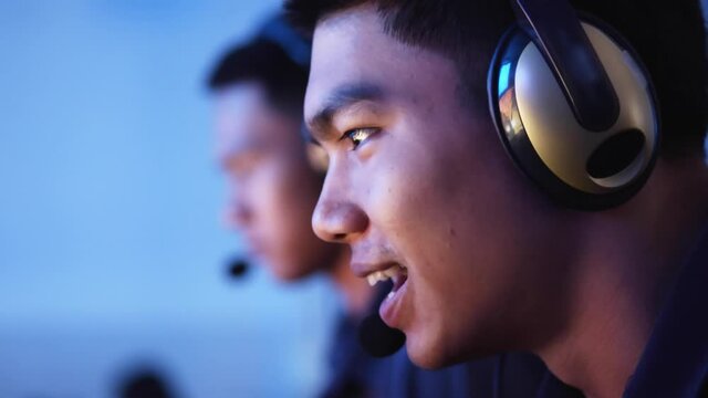 The face and eyes of a gamer, a young Asian boy, is playing a thrilling online game at an internet cafe with the reflected light on his face.