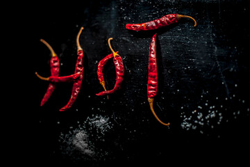 HOT written on a black surface with the help of some red hot chilies. Top shot of red hot chilies making hot word.