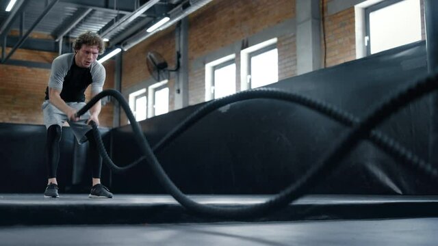 Aggressive kickboxer doing workout at gym. Sportsman using battle ropes