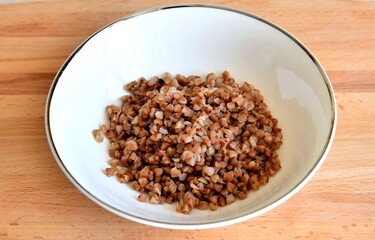 Porridge of buckwheat in a white plate on a wooden surface.