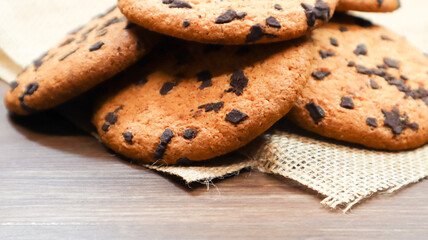 American chocolate chip cookies on a brown wooden table and on a linen napkin close-up. Traditional rounded crunchy dough with chocolate chips. Bakery. Delicious dessert, pastries. Rural still life.