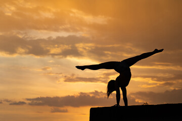 Flexible girl doing exercise on sky background during dramatic sunset