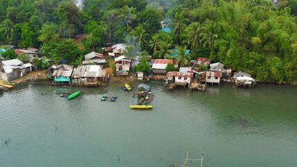 Fishing village with boats and slums with wooden houses, aerial drone. Houses community standing in water in fishing village. Luzon, Philippines.