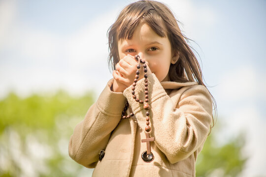 Little Child Girl Praying With Wooden Rosary.