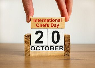 Male hand puts a block with the inscription 'International Chefs Day' on cubes with the date october 20. Beautiful wooden table, white background, copy space.