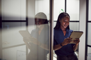 Evening Shot Of Businesswoman Standing In Corridor Of Modern Office Using Digital Tablet