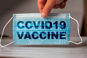 hand holds a medical and protective mask with the word COVID19 VACCINE. Concept of coronavirus quarantine. Prevent or stop the spread of the COVID-19 worldwide.