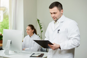 Fototapeta premium A surgeon with bristles in a white coat holds a black clipboard with documents.
