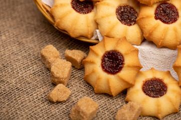 Homemade pastry cookies with jam and pieces of brown cane sugar on a background of homespun fabric with a rough texture, close-up, selective focus.