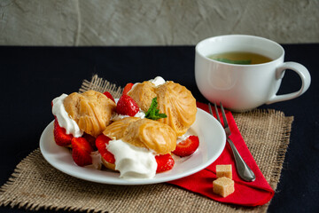 mouthwatering eclairs with ice cream, whipped cream and fresh strawberries with a cup of green tea,...