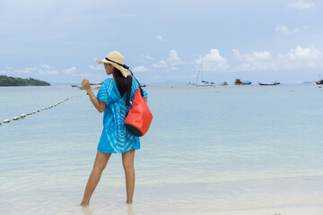 Woman in blue dress and carrying waterproof red bag , Stand on the white beaches of Phi Phi Island...