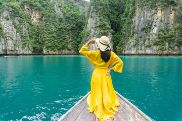 Beautiful woman in bright yellow dress, wearing hat with black bow, watching the beauty of Phi Phi Island on local longtail boat, Krabi, Thailand.