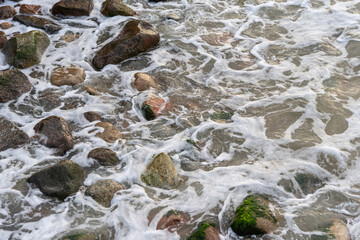 Rocks on the beach are washed by the sea wave.