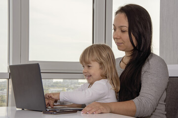 Mom and little daughter are sitting at a laptop. Concept:development and education of children using the Internet, modern concepts, work at home.