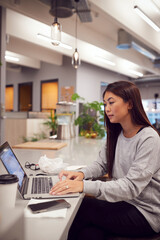 Businesswoman Working On Laptop In Kitchen Area Of Modern Office