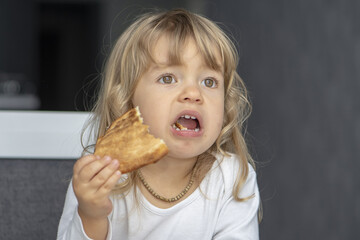 A little girl sits with her mouth open at the kitchen table and eats pizza.