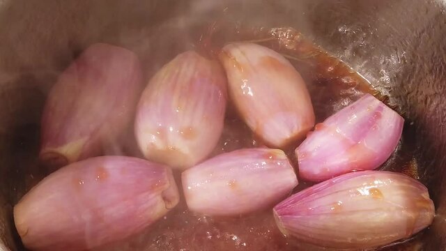 Slow motion high angle of pouring balsamico vinegar over whole shallots sizzling in hot oil in stainless steel pot_2