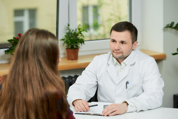 A serious doctor in a white lab coat is sitting at a desk and thinking about the treatment of a...