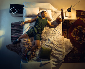 Goal. Top view of young professional basketball player sleeping at his bedroom in sportwear with ball. Loving his sport even more than comfort, playing match even if resting. Action, motion, humor.