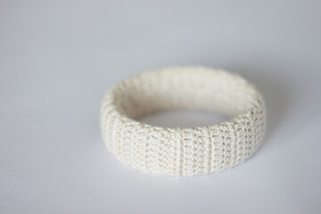 White bracelet decorated with knitted threads on a light background. 