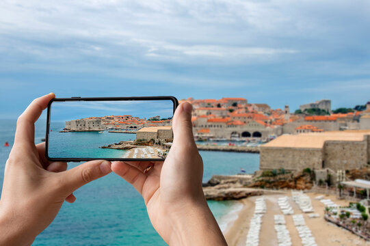 Tourist taking photo of Dubrovnik fortress walls, beach and turquoise water. Famous Banje Beach with view of the Dubrovnik city walls and old town. Beautiful blue water and yellow send.